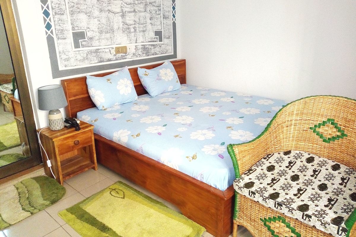 A bedroom with a bed, a nightstand, a lamp, a chair, and a wall with a map.