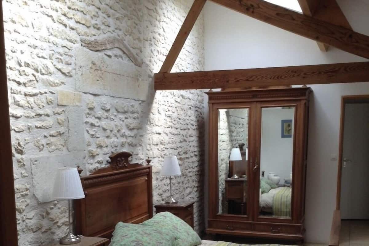 Ein Schlafzimmer mit Steinwand, Holzbalken, einem Bett mit gestreifter Decke, zwei Nachttischen mit Lampen und einem Spiegel.