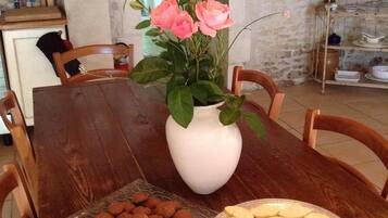 A dining table with a white vase of pink roses, a plate of cookies, and a rustic kitchen setting.