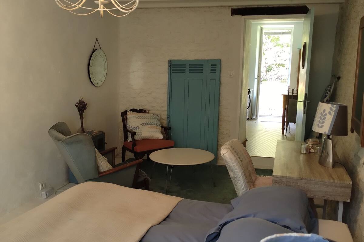 Ein Schlafzimmer mit einem Bett, einem kleinen runden Tisch, einem Sessel, einem blauen Kleiderschrank und einer Chandeliebre.