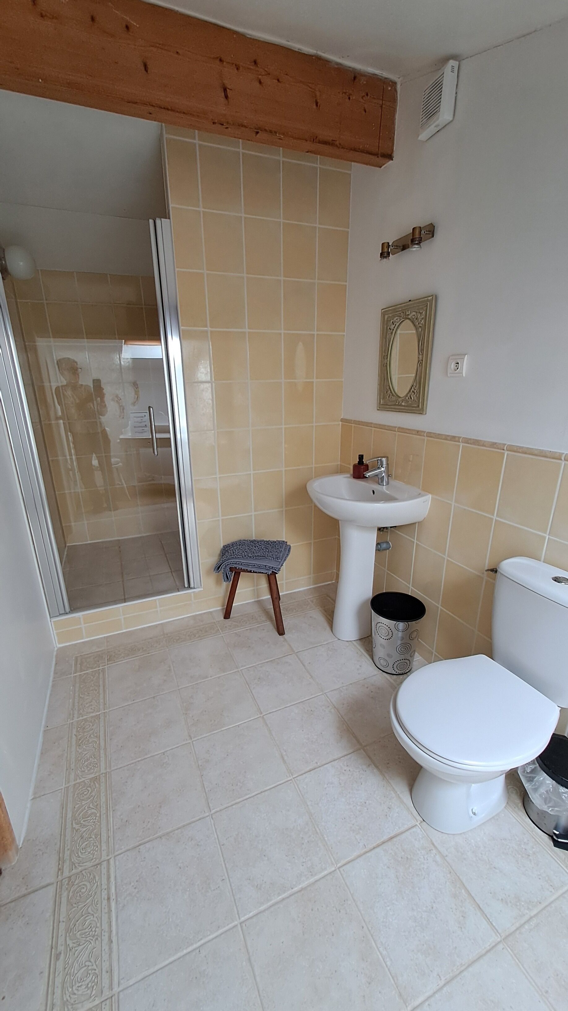 A bathroom with a shower, sink, toilet, and a small stool.