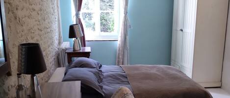 Une chambre à coucher avec un lit, un bureau, une lampe, une fenêtre avec des rideaux et un lustre.