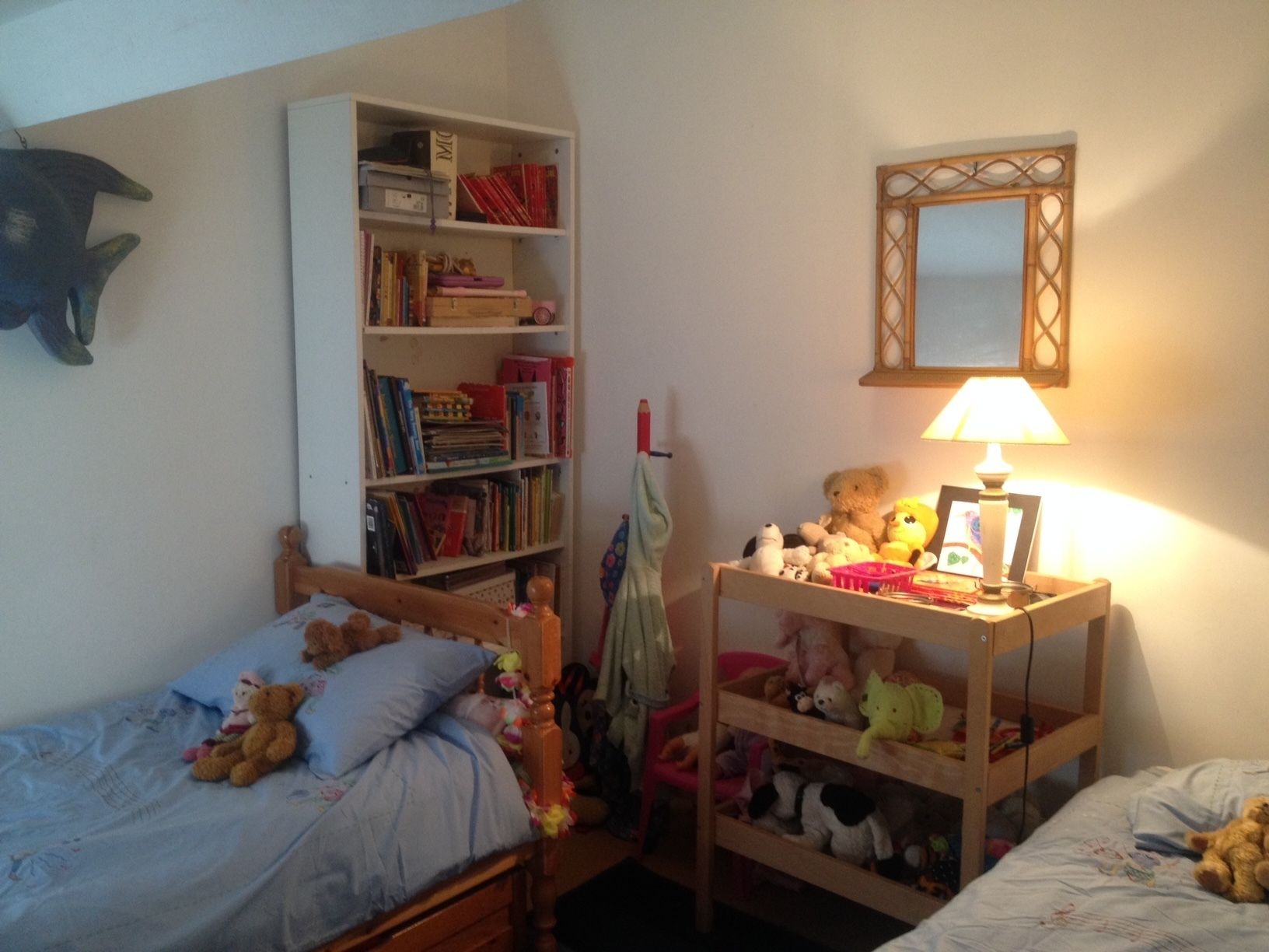 A child's bedroom with a bed, a bookshelf, a desk with a lamp, and a mirror on the wall.