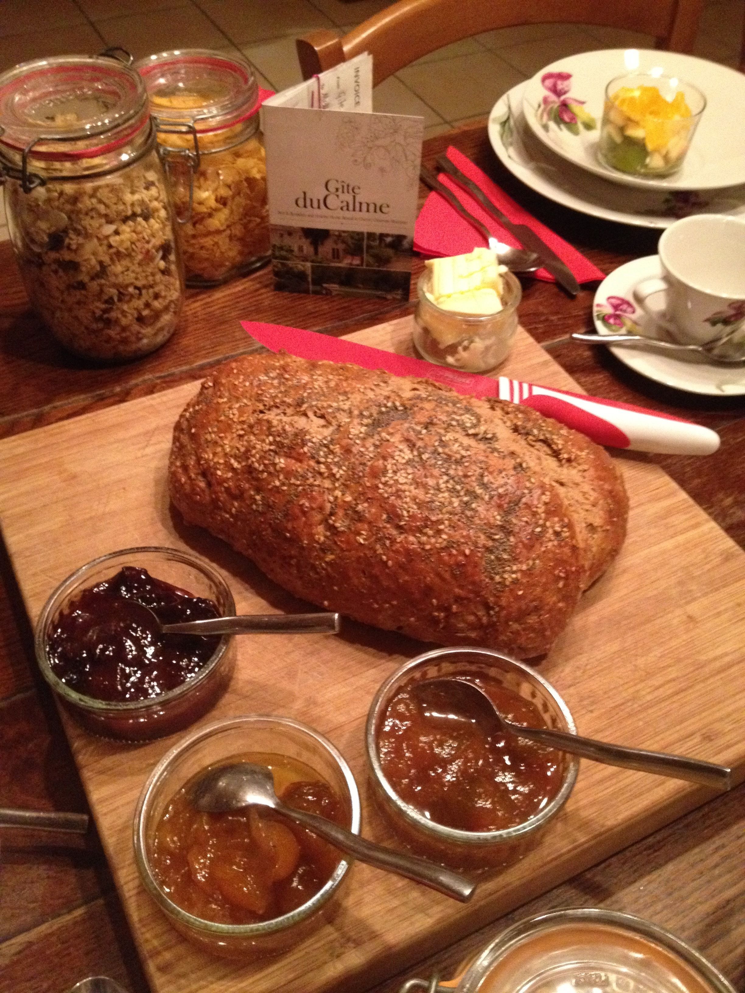 Une miche de pain sur une planche à découper en bois, accompagnée de plusieurs pots de confitures et d’une pancarte indiquant « Gîte du Calme ».