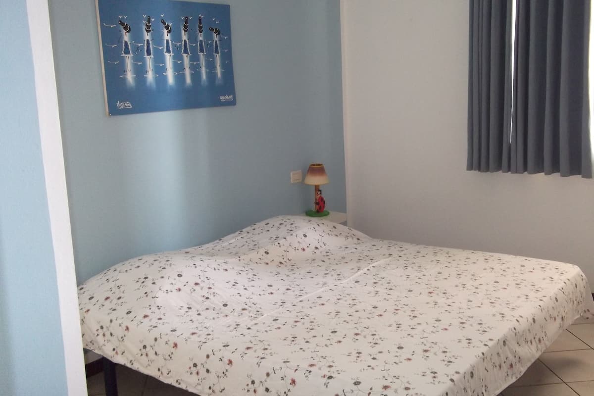 Een kamer met een bed, een aan de muur hangend kunstwerk, een lamp en een raam met gordijnen.