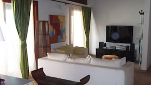 Un salon avec un canapé blanc, un banc, un téléviseur et un tableau au mur.