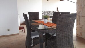 Un coin repas avec une table en verre, des chaises en osier et une plante en pot.
