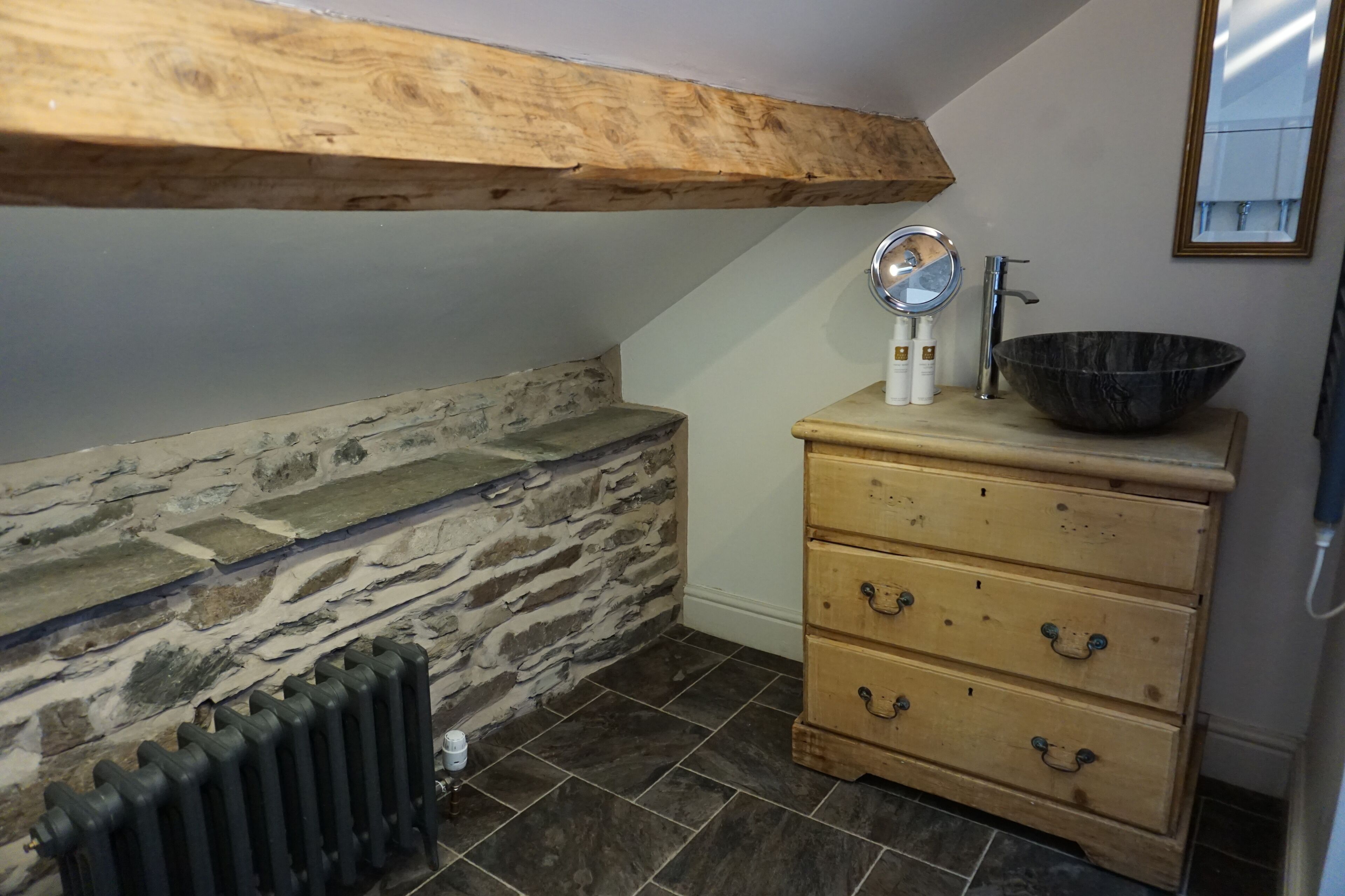 Ein Badezimmer mit einer Steinswand, Ablage aus Holz, einem Waschbecken und einem Spiegel.
