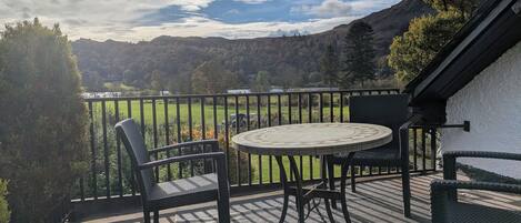 A balcony with a round table and two chairs, overlooking a scenic landscape with trees and hills.