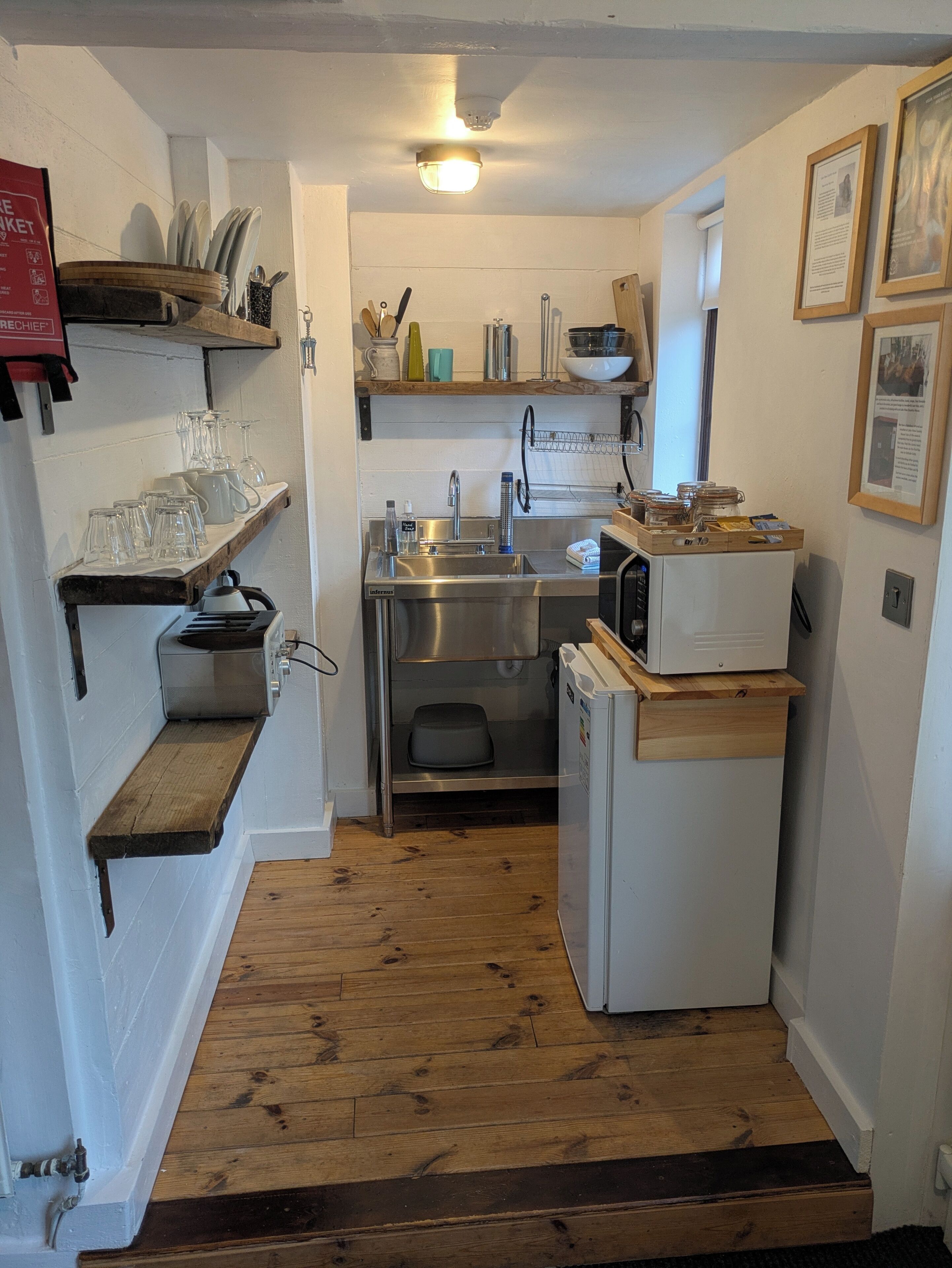 Cocina pequeña con pileta, microondas y estantes de madera.
