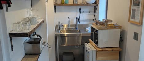 A compact kitchen with a sink, microwave, and wooden shelves.