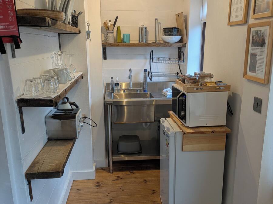Cocina pequeña con pileta, microondas y estantes de madera.
