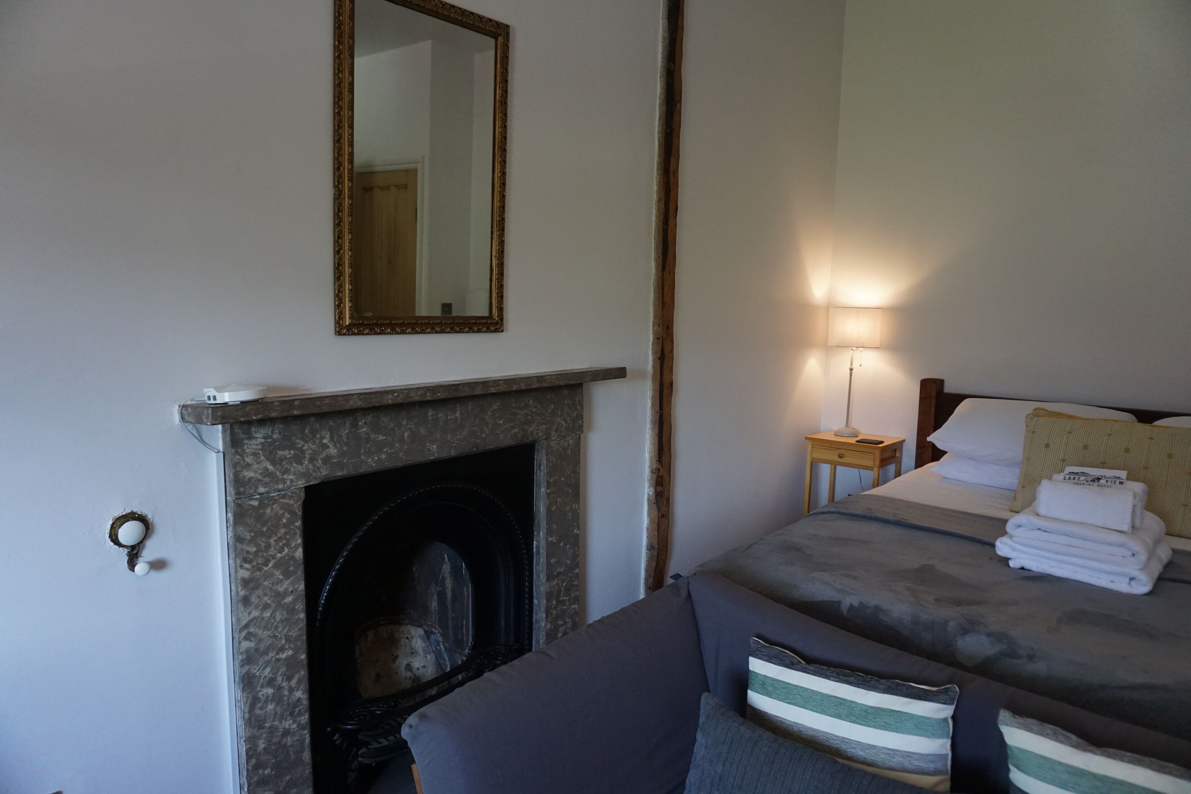 Un dormitorio con chimenea, una cama con toallas ordenadas, una lámpara de noche y un espejo en la pared.