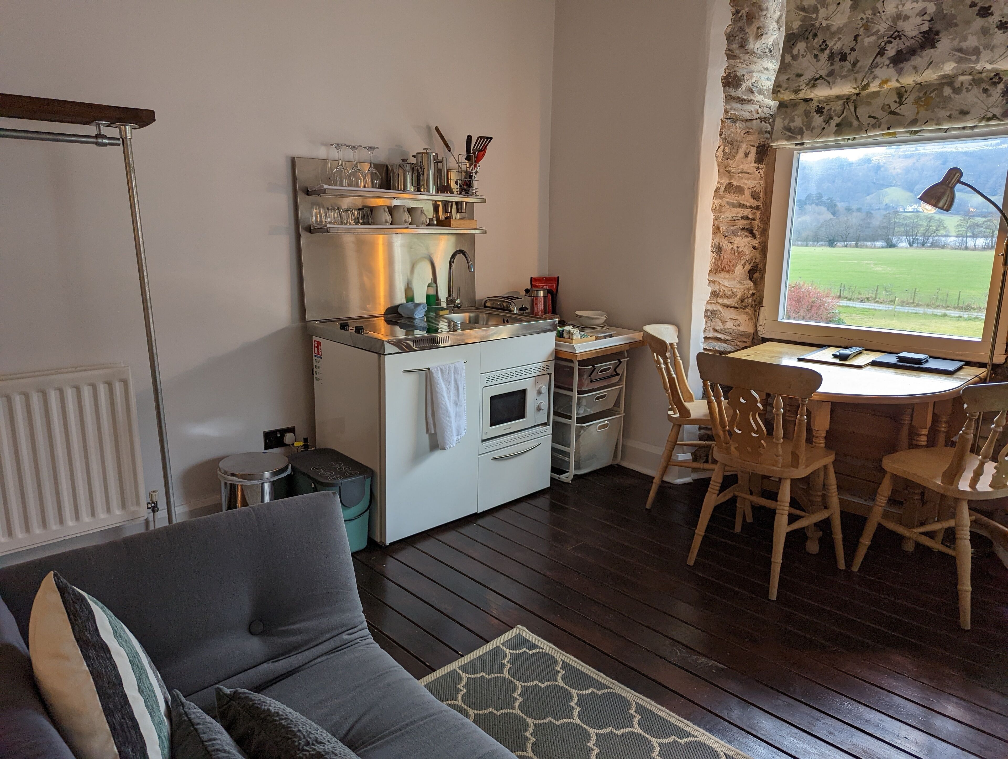 Una cocina compacta con horno empotrado, un lavamanos y una pequeña zona de comedor con sillas de madera.