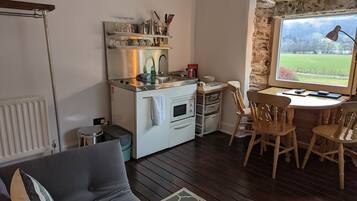 Una cocina compacta con horno empotrado, un lavamanos y una pequeña zona de comedor con sillas de madera.