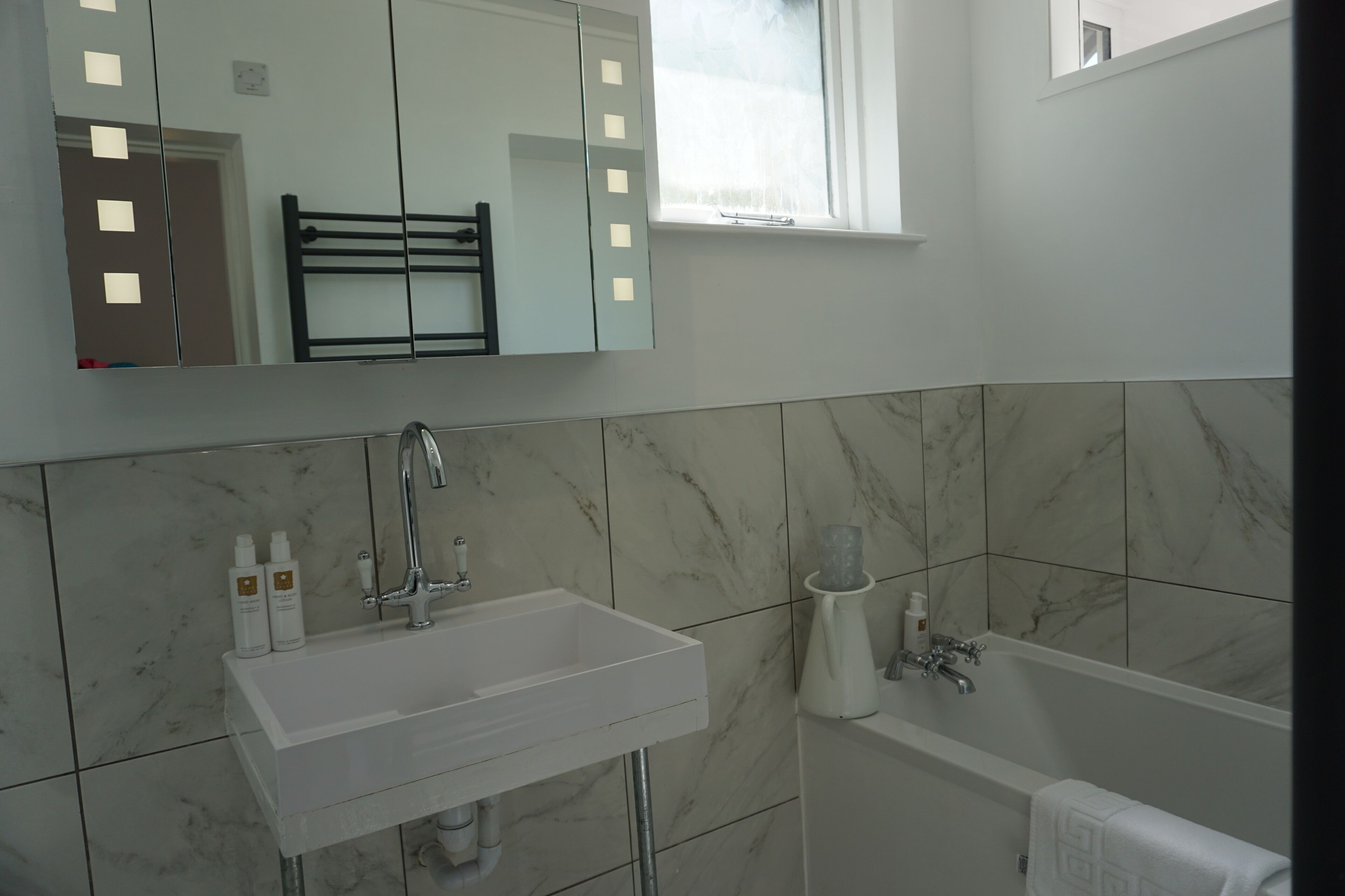 A bathroom with a white sink, a mirror, a towel rack, and a bathtub.