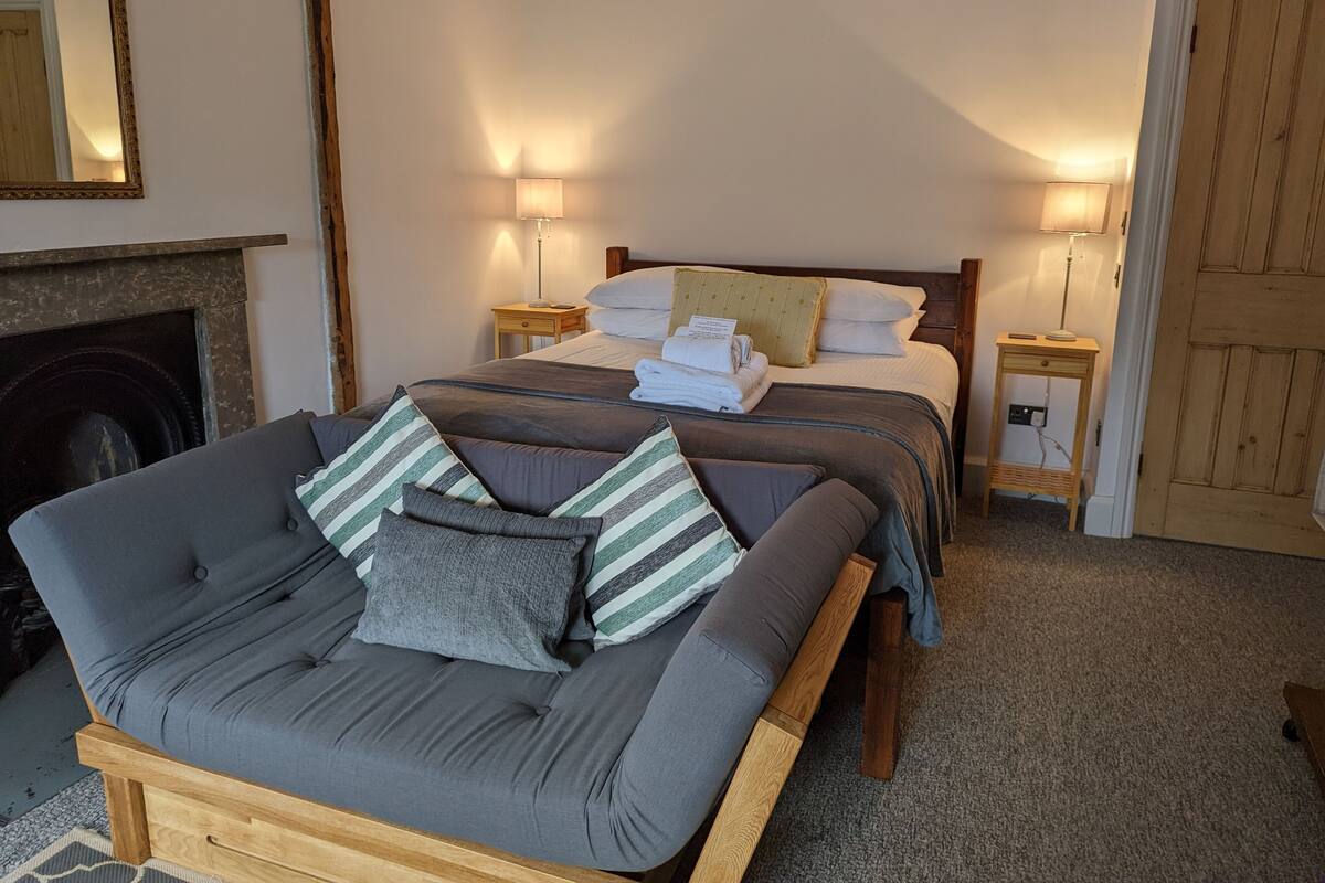 A cozy bedroom with a bed, bedside lamps, a sofa, and a fireplace.