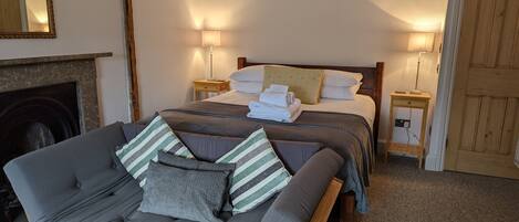 A cozy bedroom with a bed, bedside lamps, a sofa, and a fireplace.