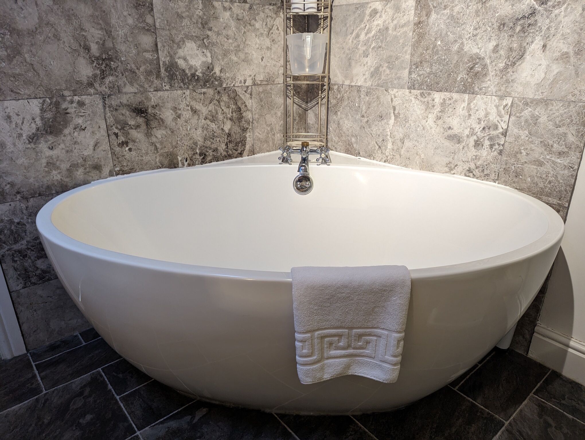 Une grande baignoire sur pieds, avec une serviette posée dessus, placée devant un mur en pierre.