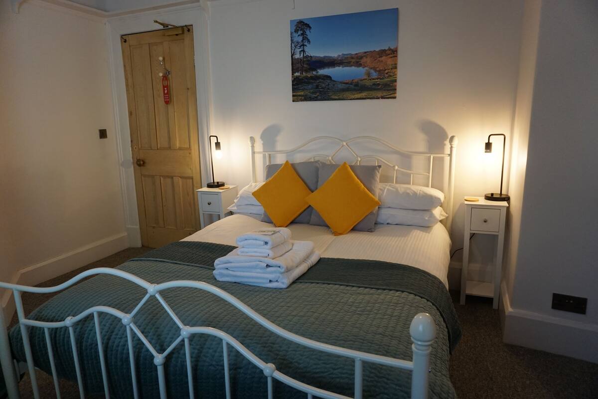 A neatly made bed with folded towels, a wooden door, and a landscape painting on the wall.