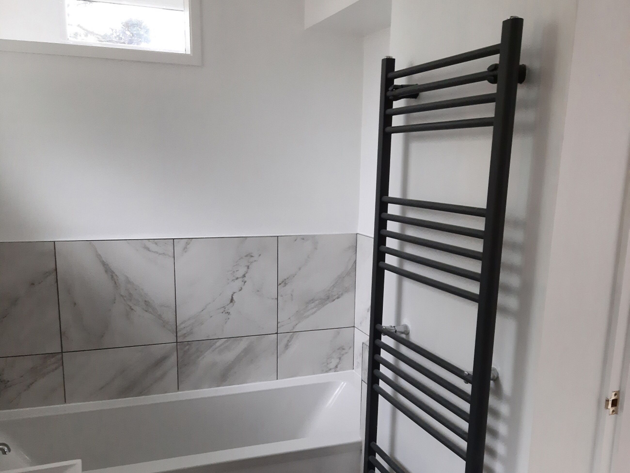A bathroom with a white bathtub, marble tiles, and a black towel rack.