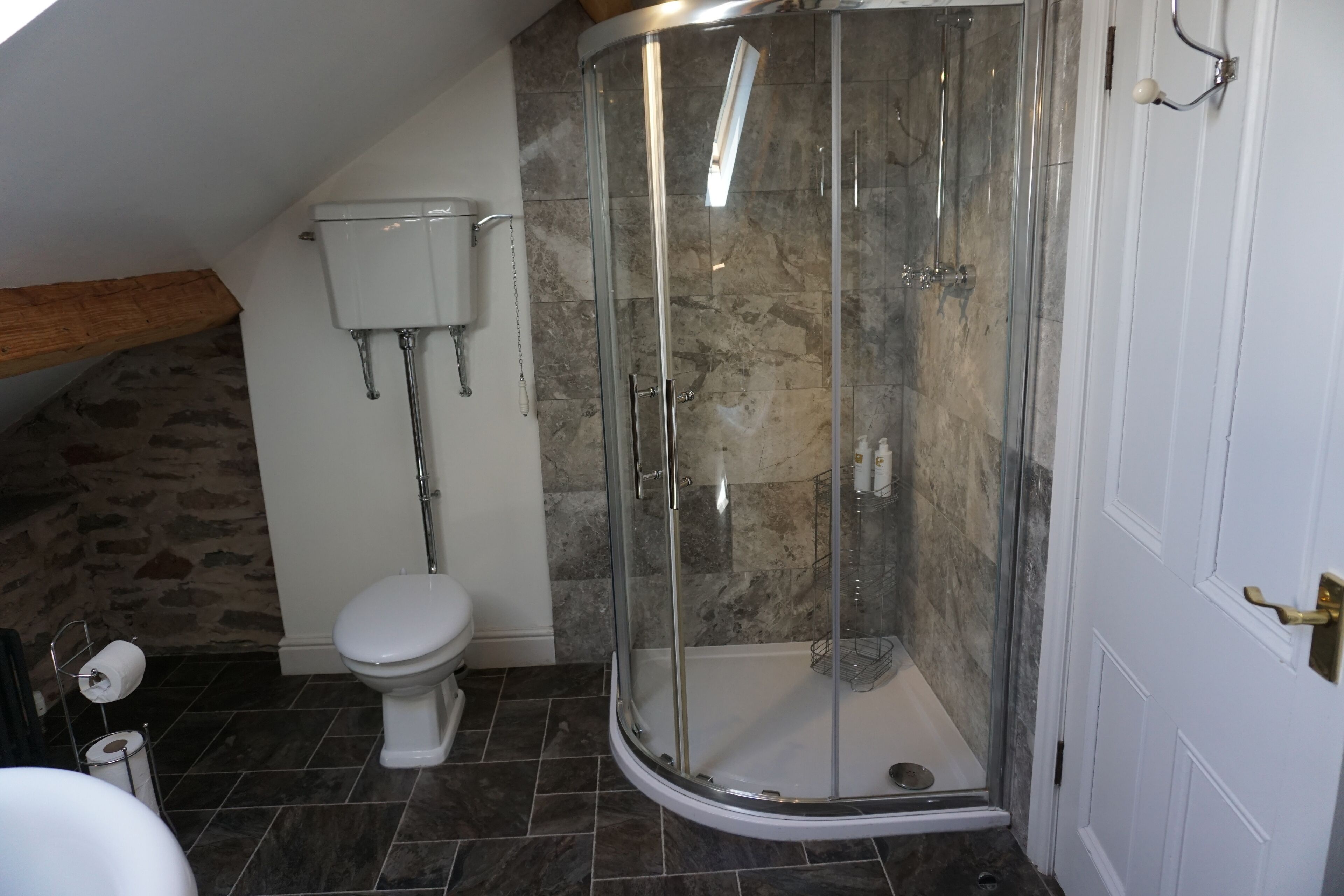 Un baño con cabina de ducha de vidrio, inodoro y pared de piedra.