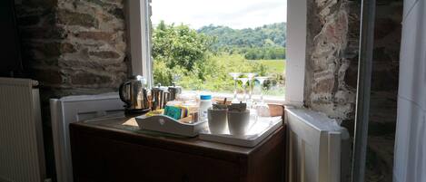 Una cocina con pared de piedra rústica, encimera de madera y vistas a un paisaje verde a través de una ventana.