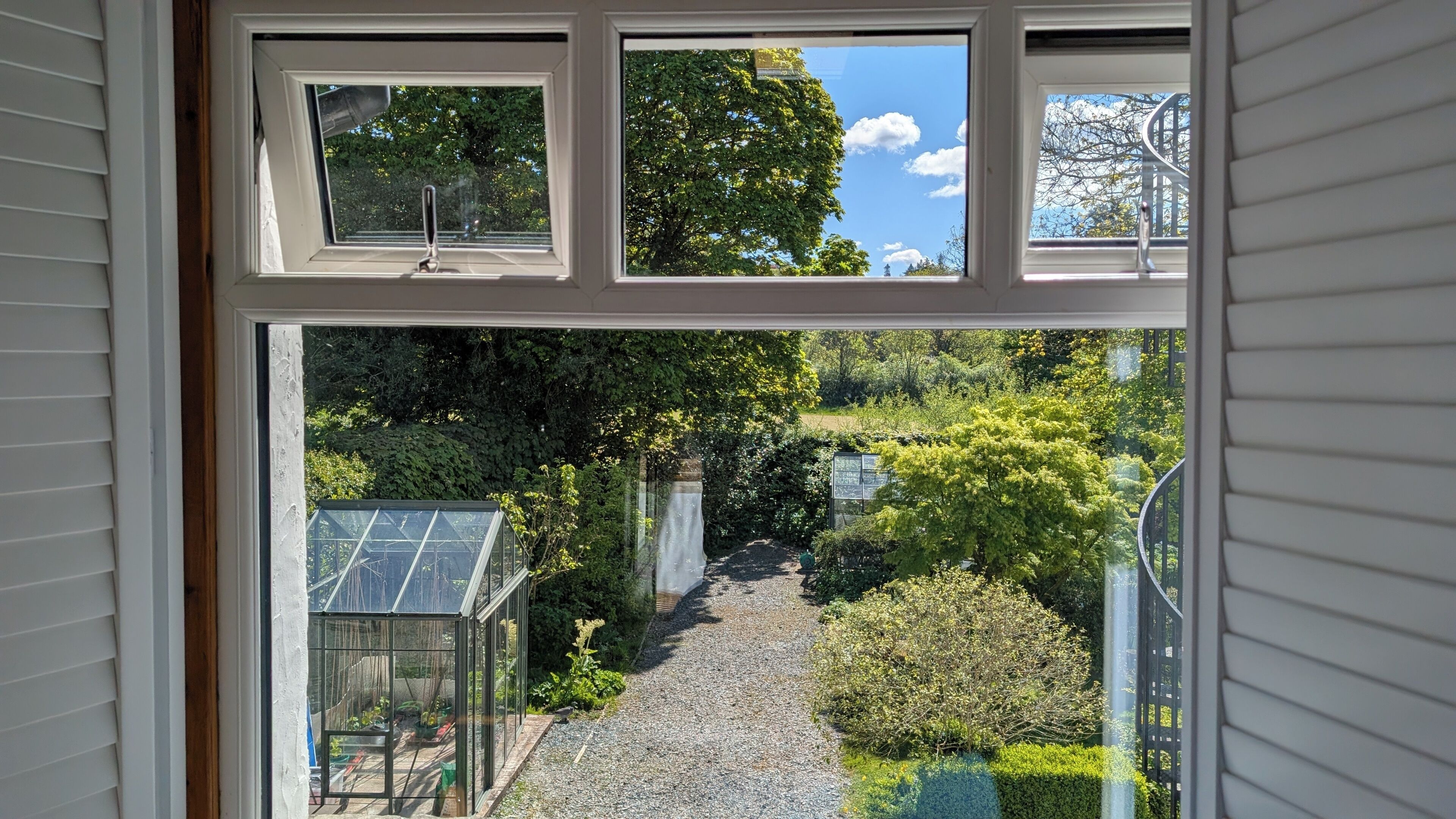Vista a través de una ventana, con un sendero en el jardín que lleva a un invernadero.