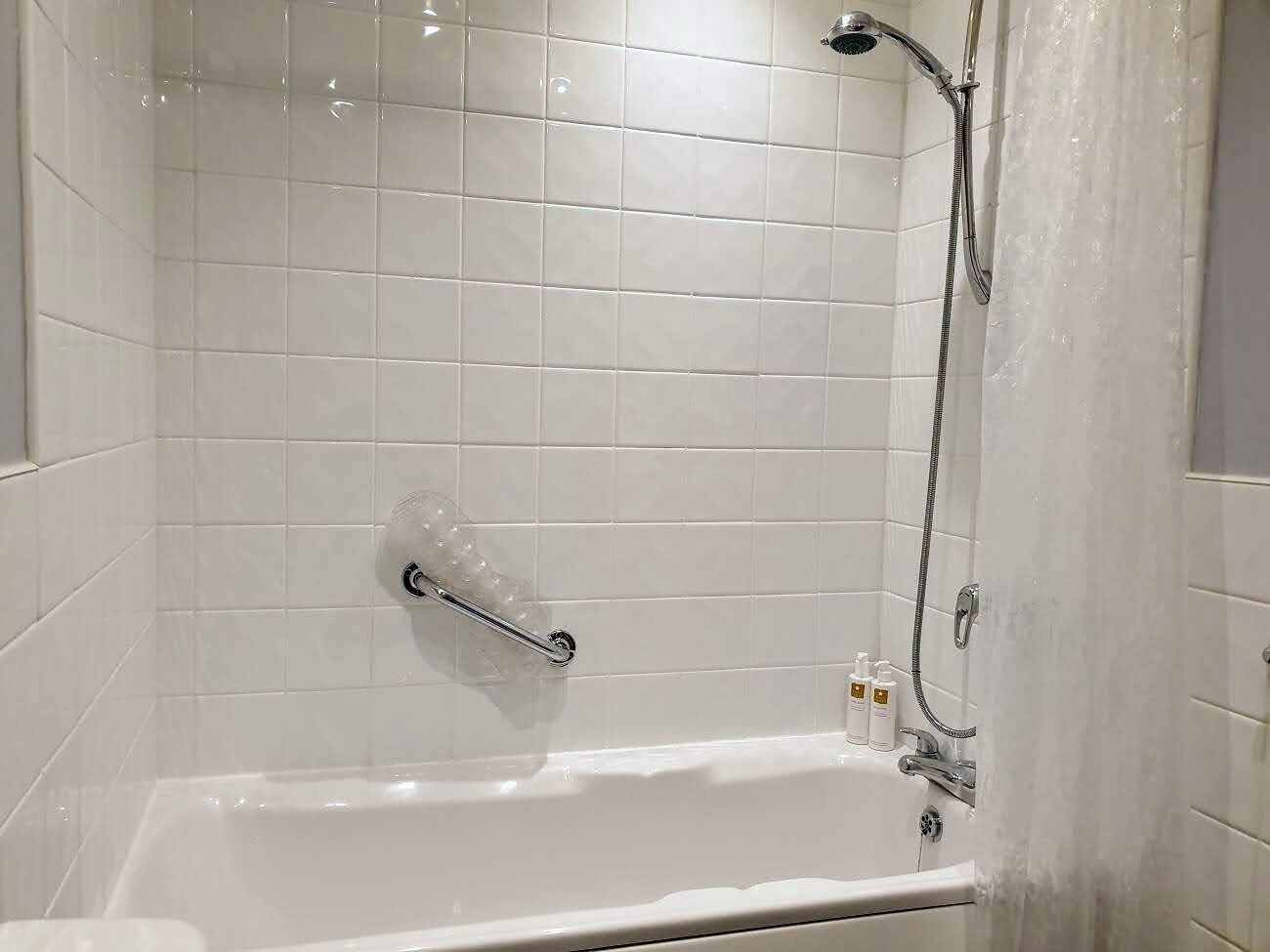 A white-tiled bathroom with a bathtub, a handheld showerhead, and a handheld shower attachment.