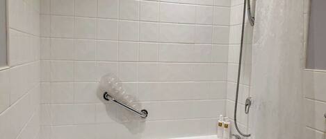 A white-tiled bathroom with a bathtub, a handheld showerhead, and a handheld shower attachment.