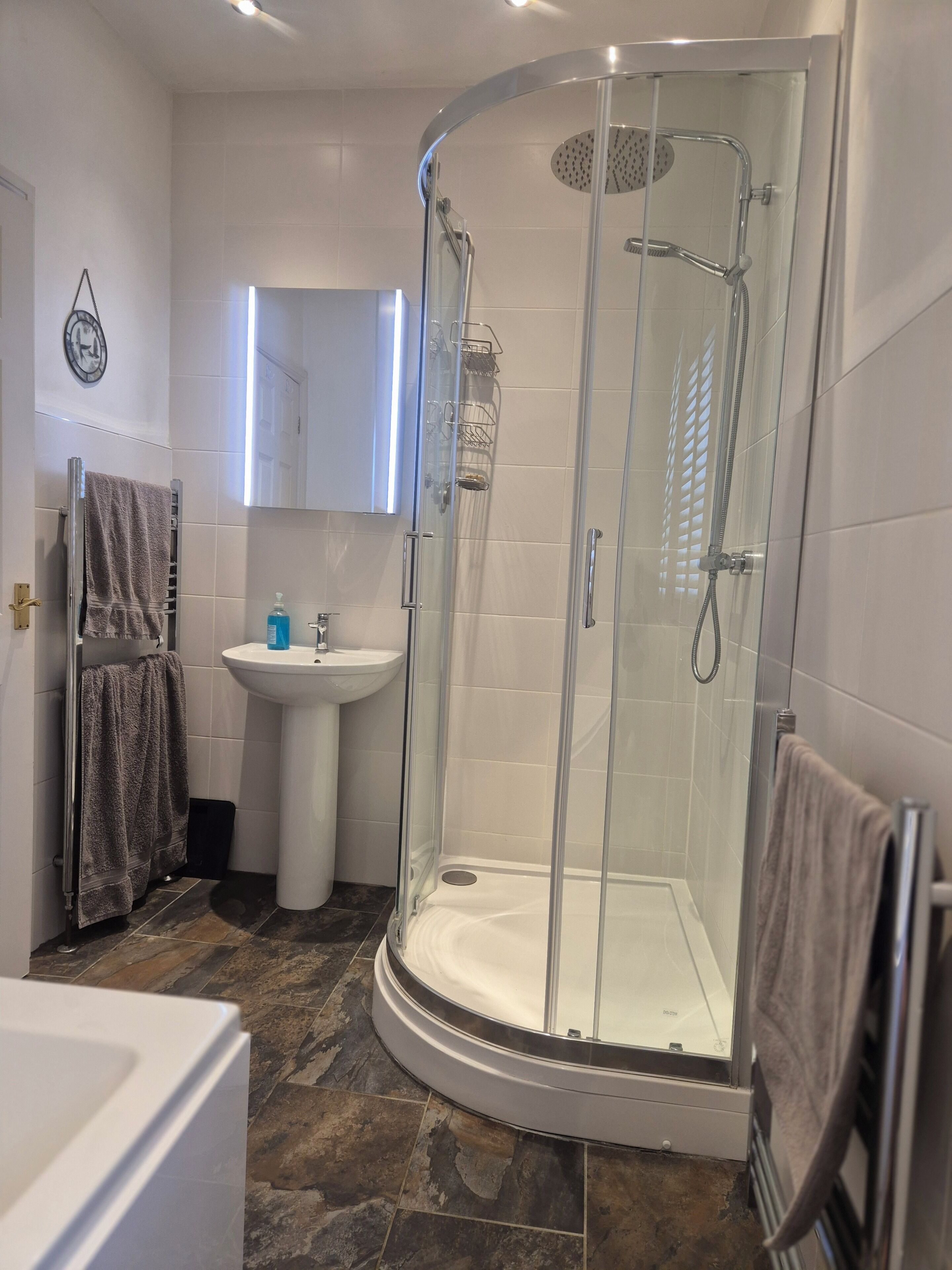 Un bagno con doccia vetrata, lavabo su piedistallo e porta asciugamani.