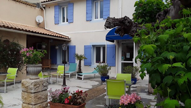 A courtyard with outdoor seating, potted plants, and a building with blue shutters. - Hôtel du Viaduc (Tarascon)