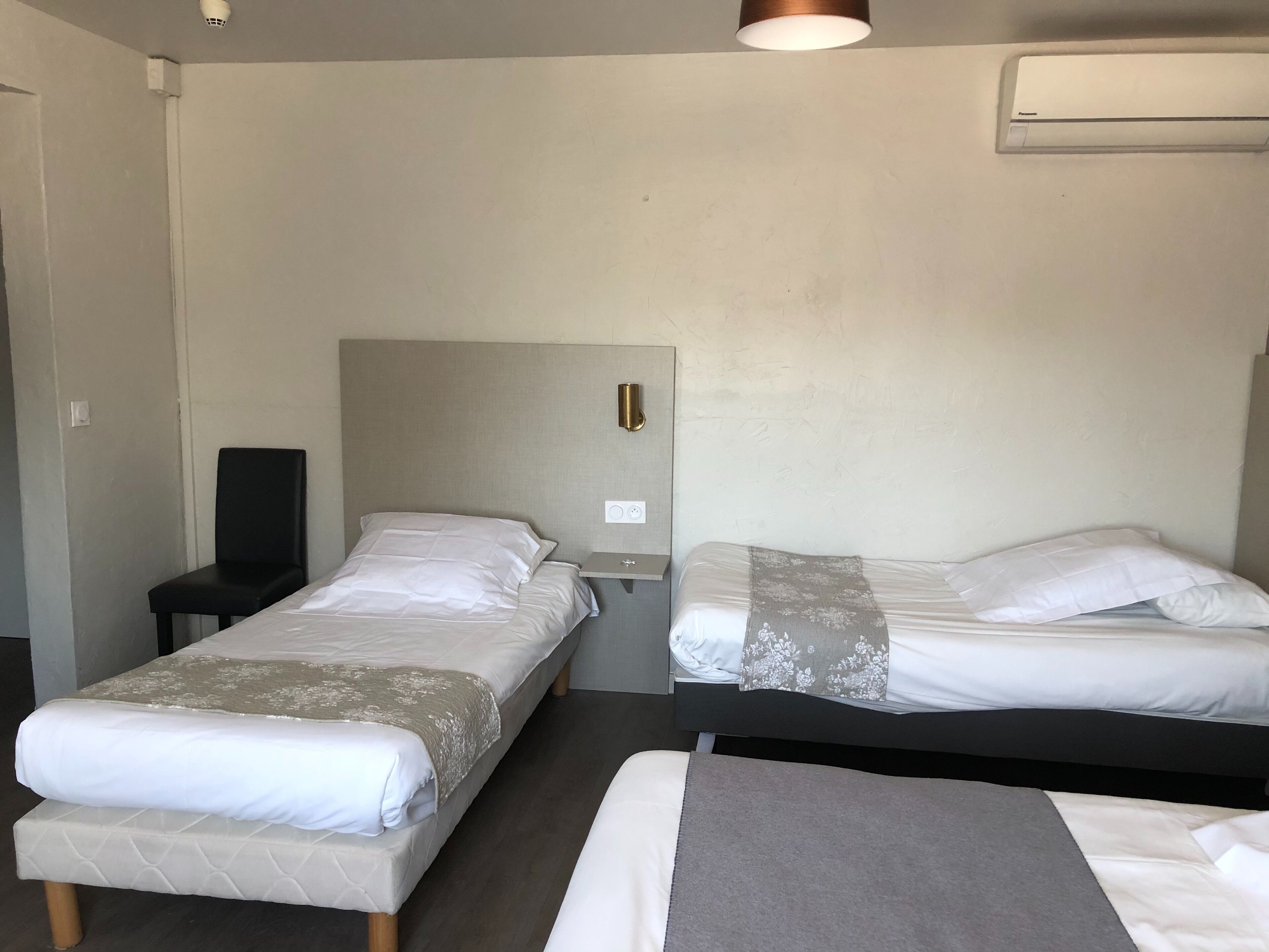 Habitación de hotel con dos camas, un escritorio, una silla y aire acondicionado instalado en la pared.