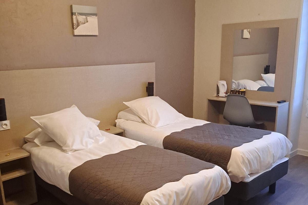 Ein Hotelzimmer mit zwei Betten, einem Schreibtisch, einem Stuhl und einem Spiegel.