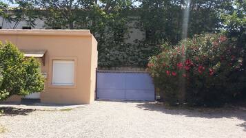 Un edificio con fachada color crema, una puerta blanca con contraventanas cerradas y un camino de entrada de grava.