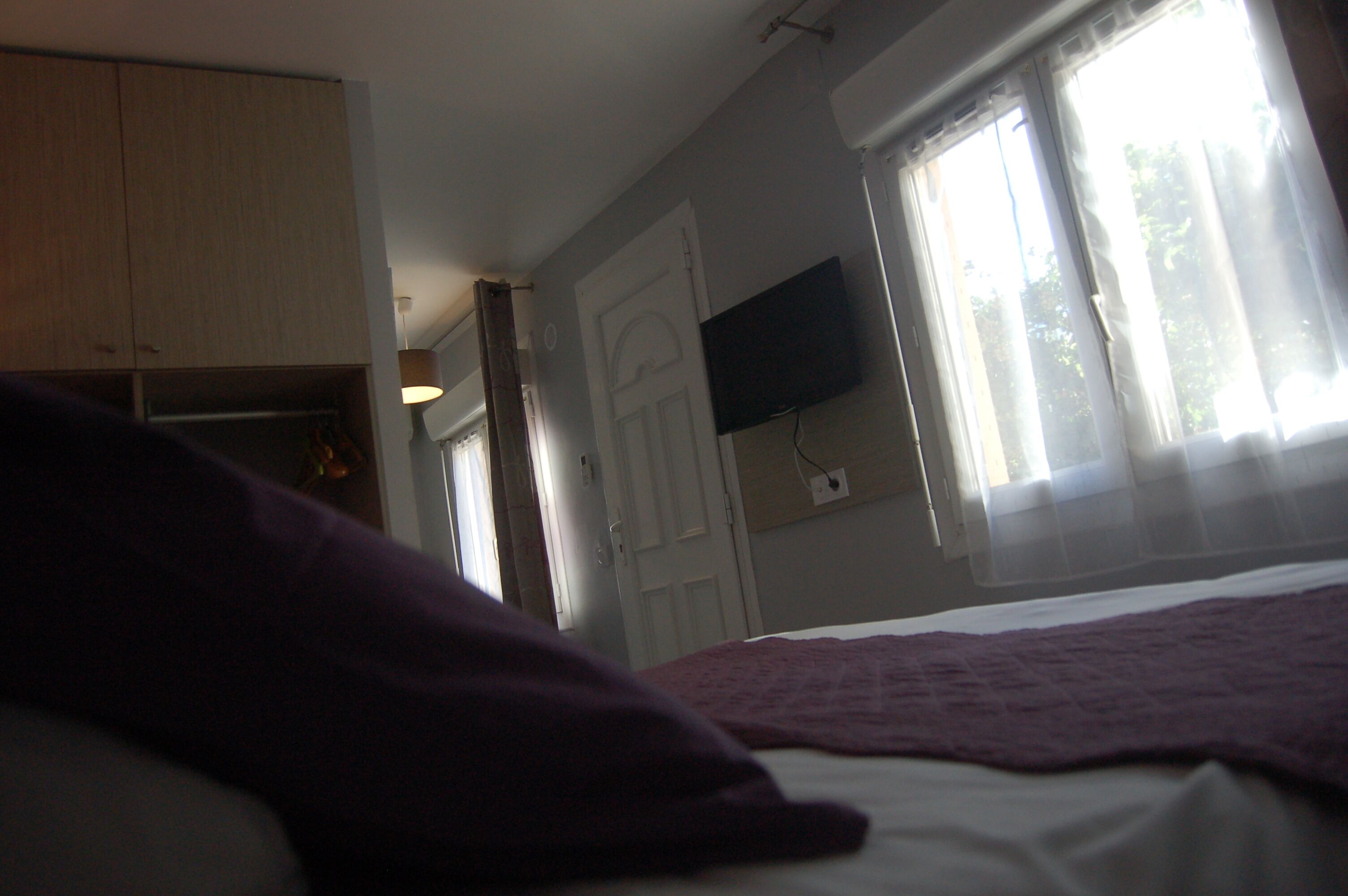 Quarto com cama, televisão fixada na parede e janela com cortinas.