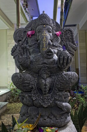 A stone statue of a deity with intricate carvings, placed outdoors with plants around it. - Sura Inn Ubud (Ubud)