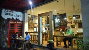A coffee shop with a red telephone booth, wooden stools, and hanging lights. - Sura Inn Ubud (Ubud)