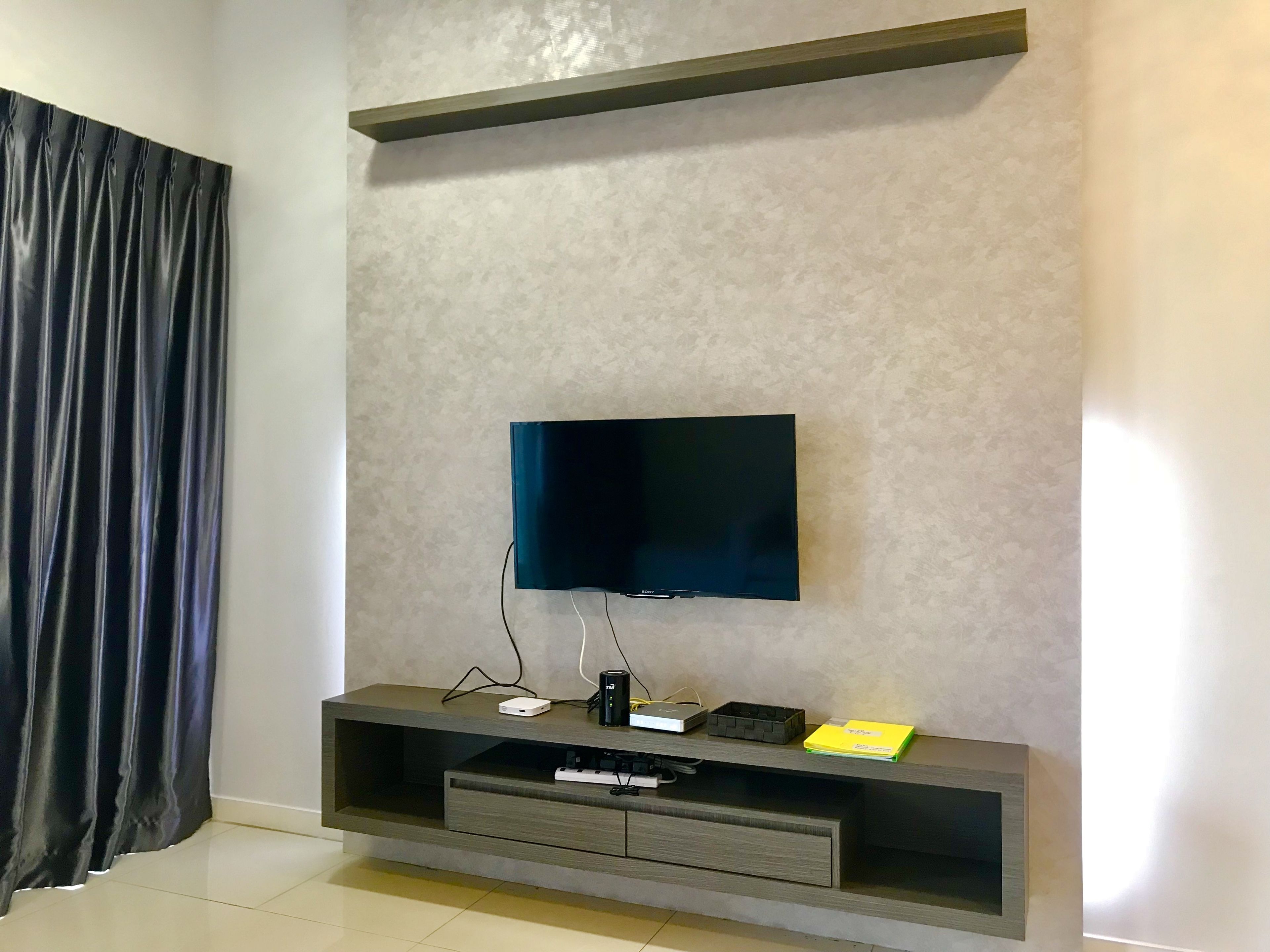 A modern living room with a flat-screen TV mounted on a textured wall, a dark wooden entertainment unit below, and a dark curtain on the left.