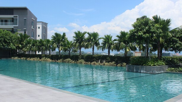 A swimming pool with clear blue water, surrounded by palm trees and a modern building in the background.