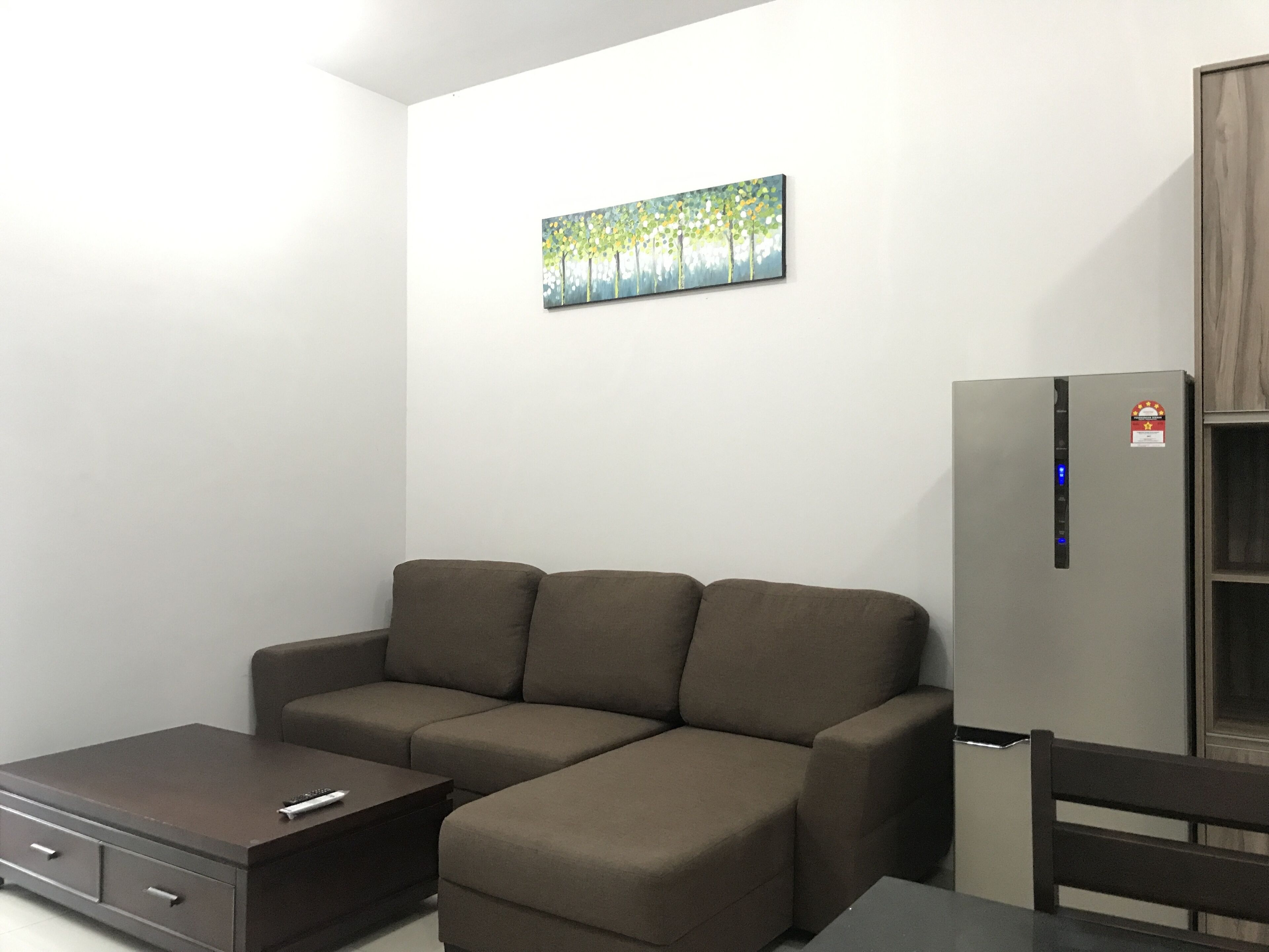 A modern living room with a sectional sofa, a small table, a cabinet, and a refrigerator.