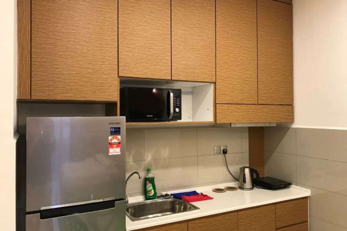 Una cocina con armarios de madera, un refrigerador de acero inoxidable, un microondas, una tetera y un lavamanos.