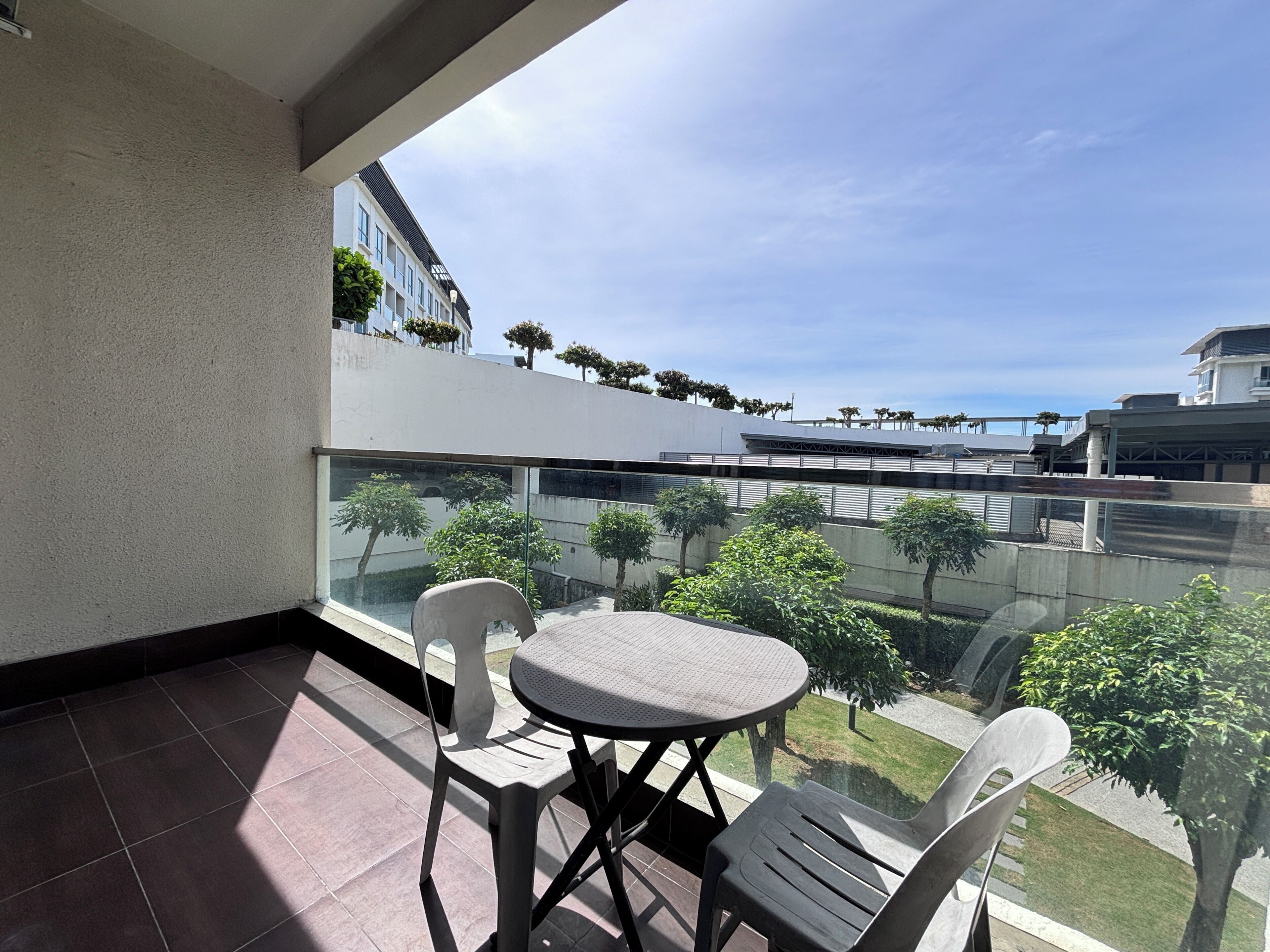 A balcony with a table and chairs, a glass railing, and a view of a building and trees.