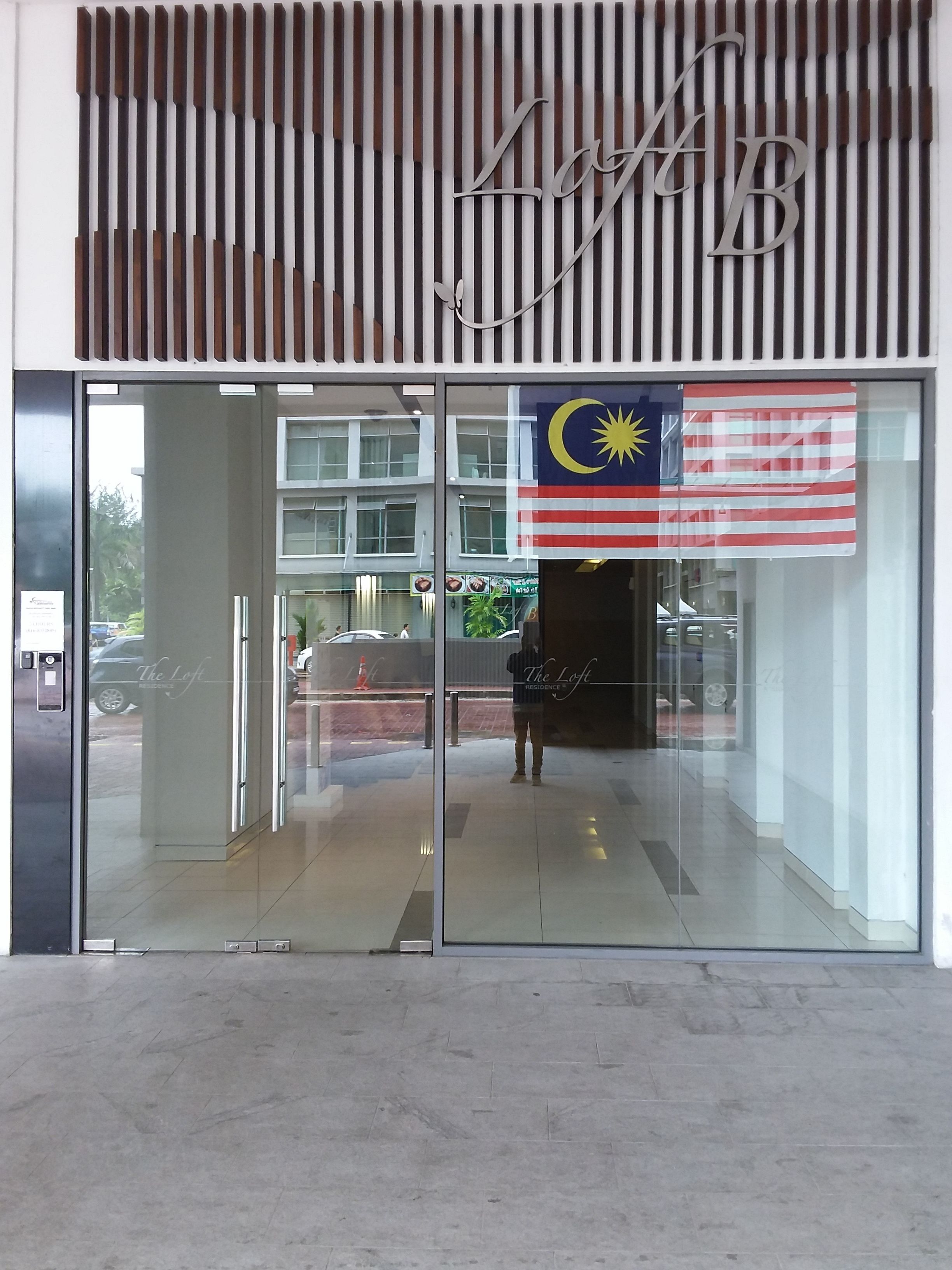 L’entrée d’un hôtel au design moderne, avec une porte en verre et un drapeau malaisien.