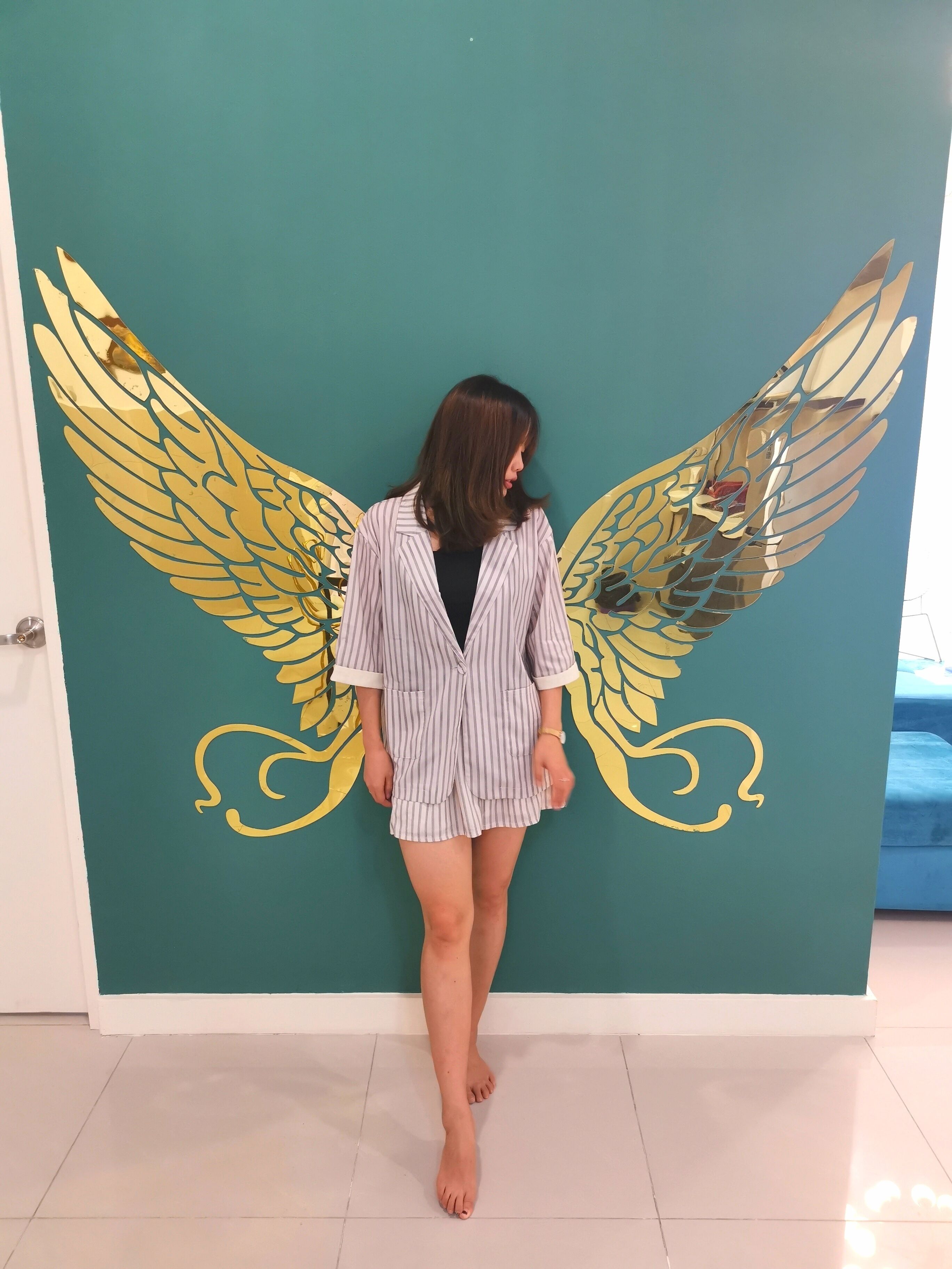 Une personne se tient devant un mur de couleur turquoise orné d’un grand motif représentant une aile dorée.