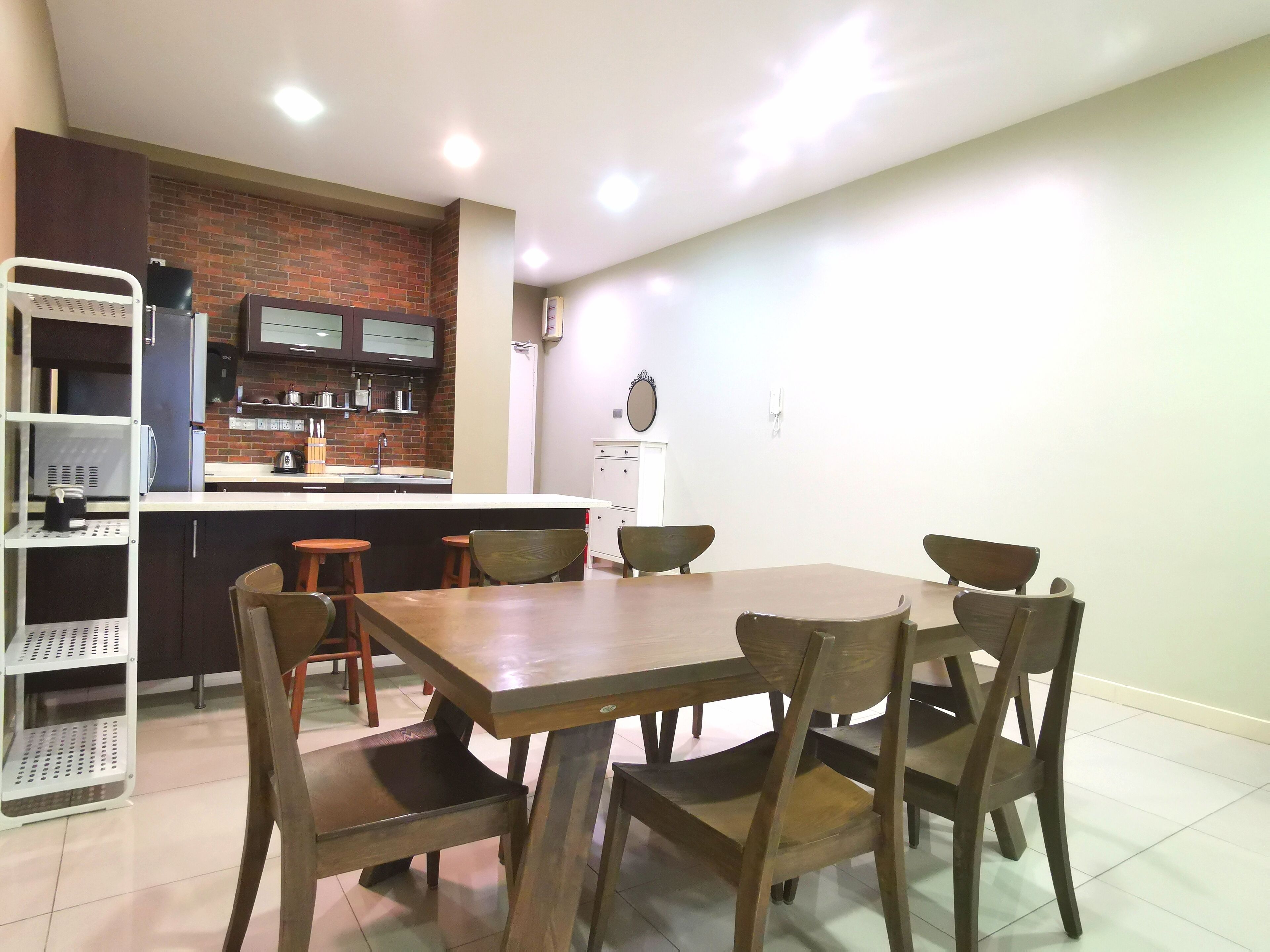 A dining area with a wooden table and chairs, a kitchen with a brick backsplash, and a white cabinet.