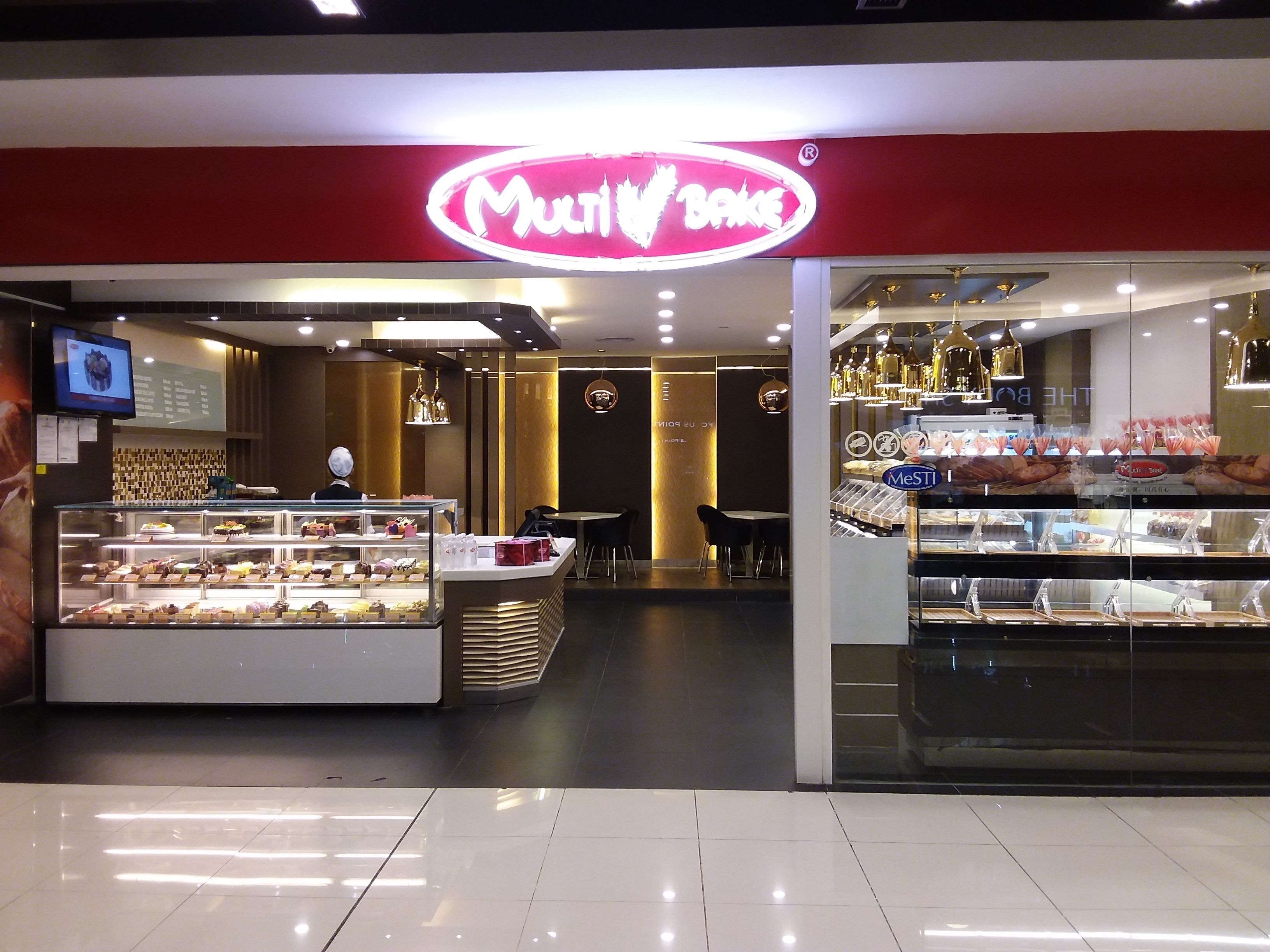 A bakery with a red and white sign, a display case with baked goods, and a seating area with tables and chairs.