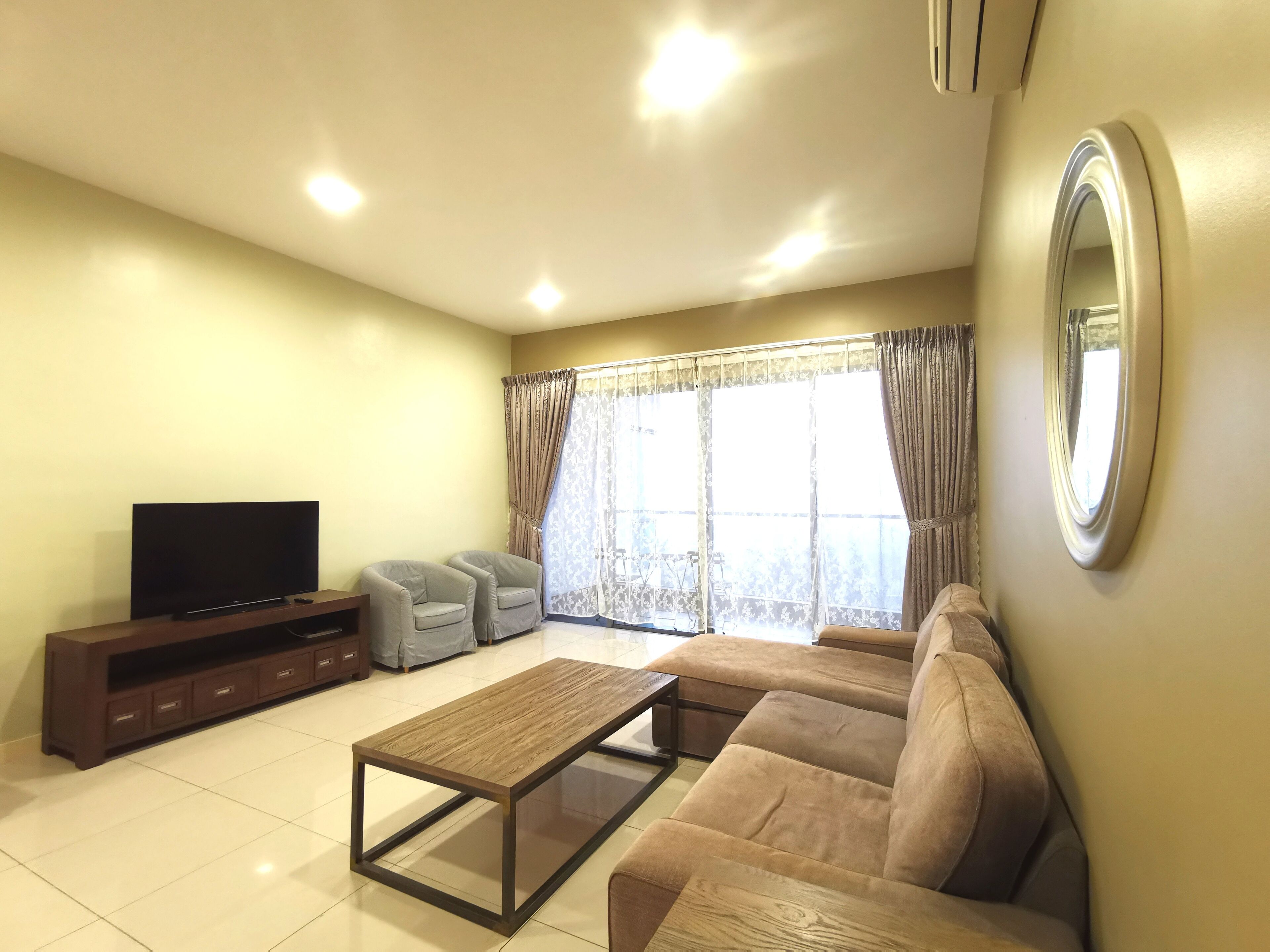 A living room with a sofa, two armchairs, a coffee table, a TV, and a large window with curtains.