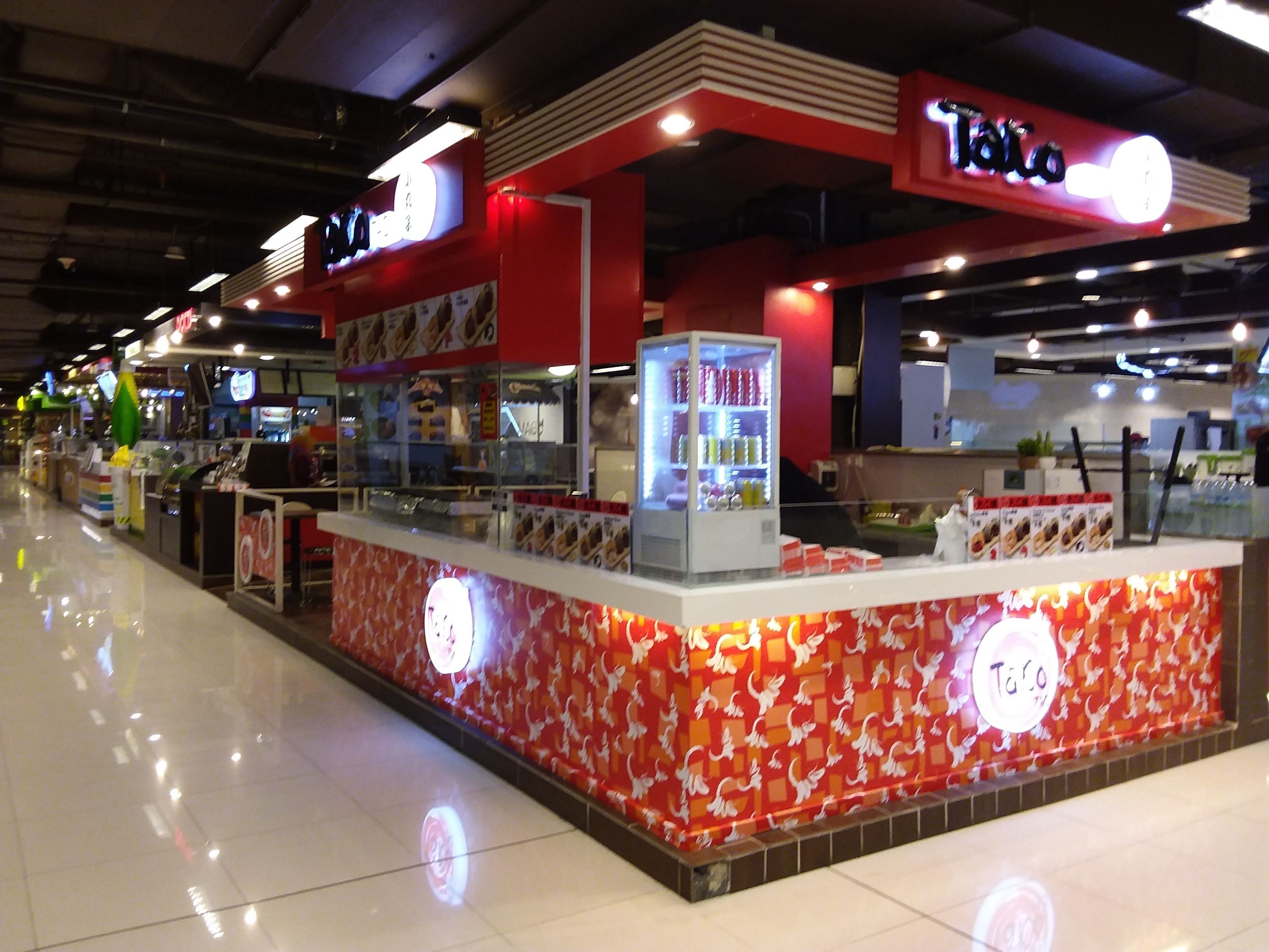 A food kiosk with a red and white color scheme, featuring a glass display case and a sign that reads "Taco".