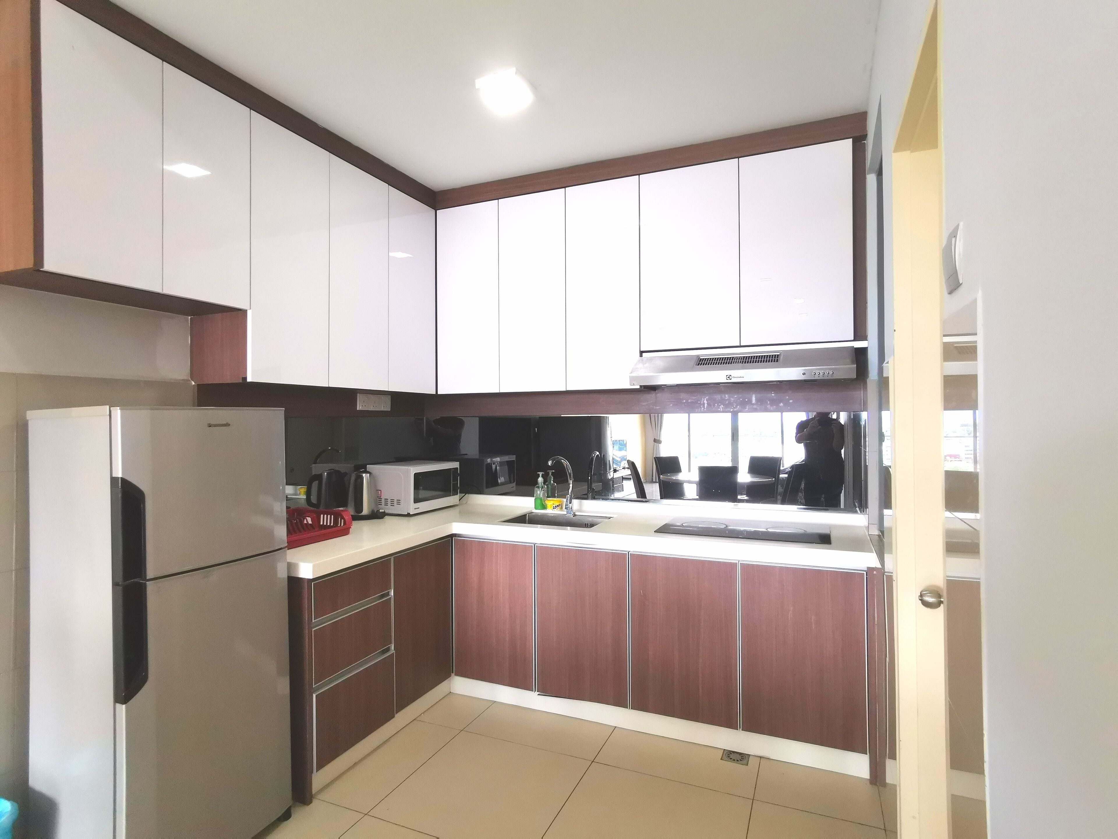 A compact kitchen with white and brown cabinets, a stainless steel refrigerator, a microwave, and a sink.